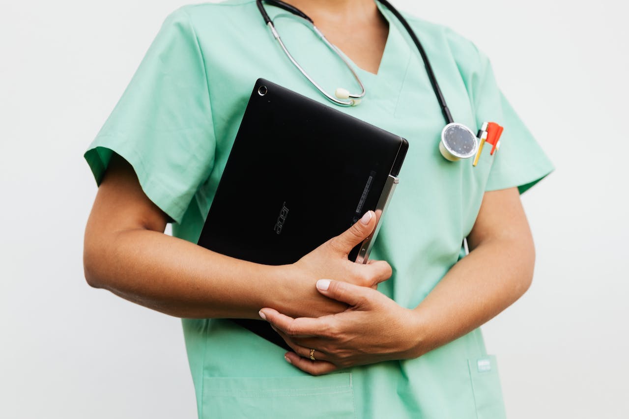 Niepełne ujęcie pielęgniarki trzymającej w rękach tablet, na szyi stetoskop.