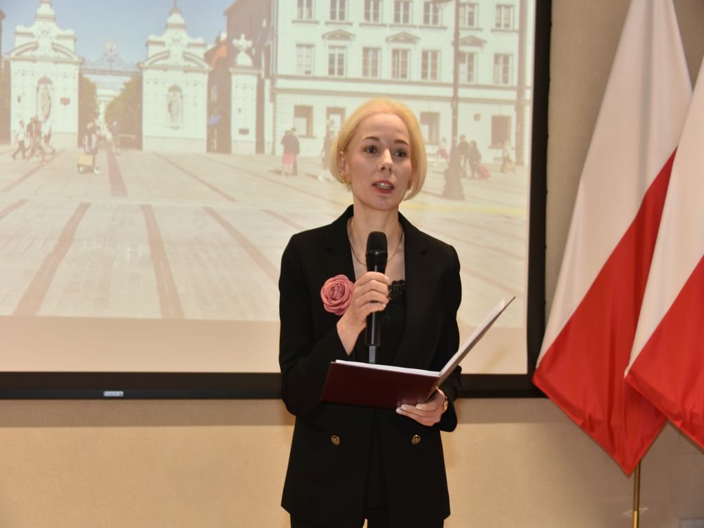 Uroczyste otwarcie Pracowni Anatomii w Wojskowym Instytucie Medycznym. Prowadząca trzyma mikrofon, za nią slajd prezentacji.