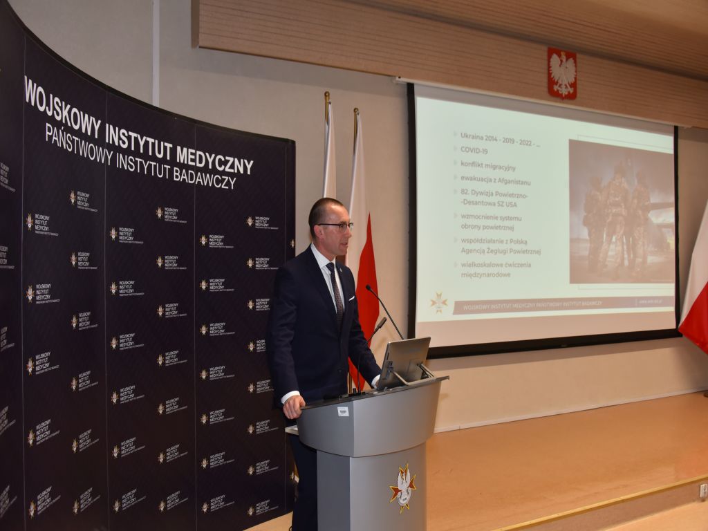 Uroczyste otwarcie Pracowni Anatomii w Wojskowym Instytucie Medycznym. Prelegent przy mównicy, za nim slajd prezentacji.