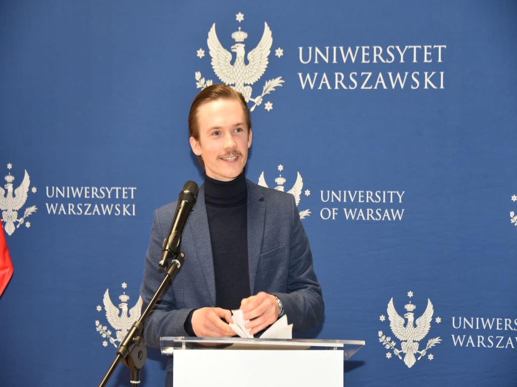 Uroczyste otwarcie Pracowni Anatomii w Wojskowym Instytucie Medycznym. Prelegent przy mównicy, za nim logo Uniwersytetu Warszawskiego.