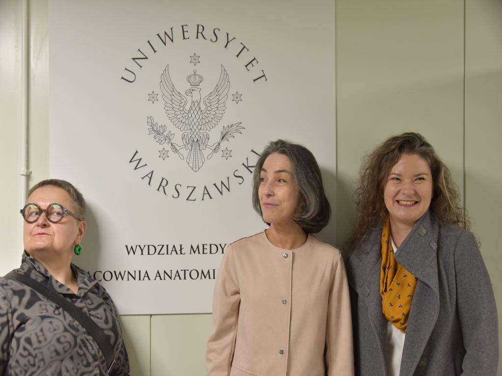 Uroczyste otwarcie Pracowni Anatomii w Wojskowym Instytucie Medycznym. Zdjęcie gości, w tle logo Uniwersytetu Warszawskiego.