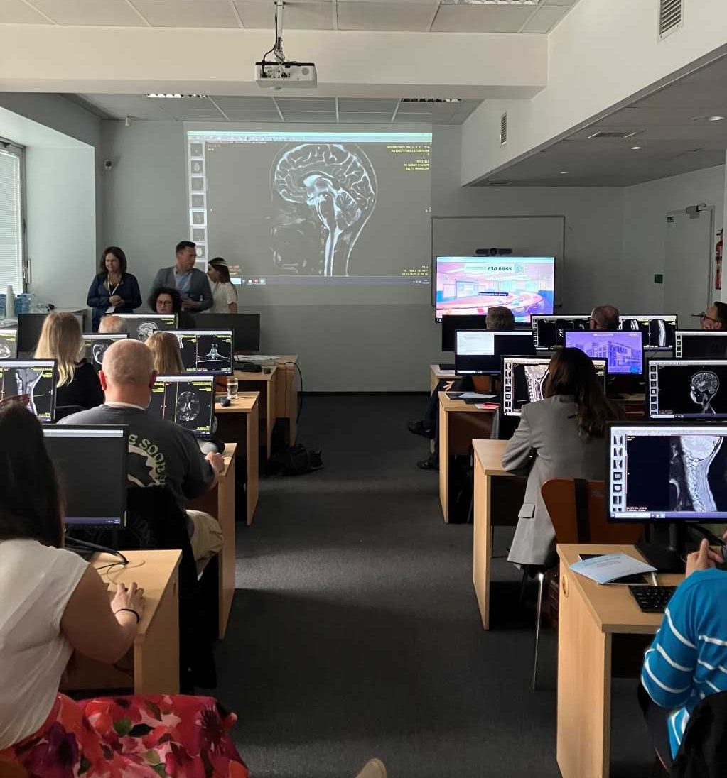 Szkolenie dla neurologów z zasad diagnostyki i leczenia stwardnienia rozsianego w wojskowym instytucie medycznym. Sala wykładowa a w niej siedzący przy komputerach słuchacze, przed nimi obraz z rzutnika przedstawiający obraz mózgu.