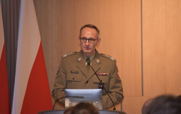 Dyrektor WIM Grzegorz Gielerak przemawia przy mównicy do zebranych gości, w tle dwie flagi Polski.