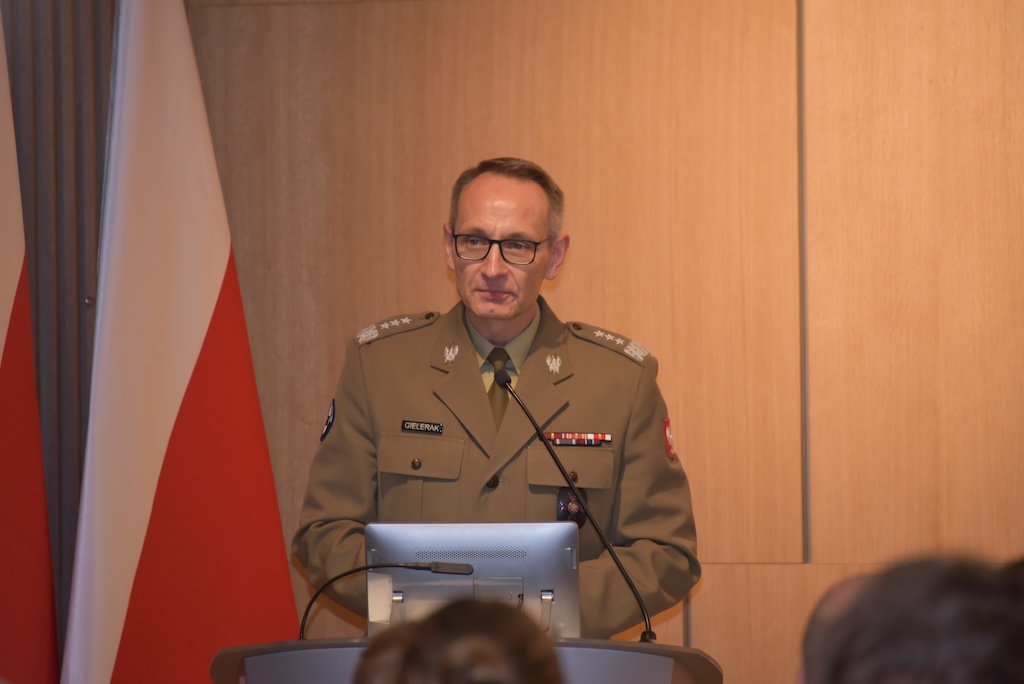 Dyrektor WIM Grzegorz Gielerak przemawia przy mównicy do zebranych gości, w tle dwie flagi Polski.