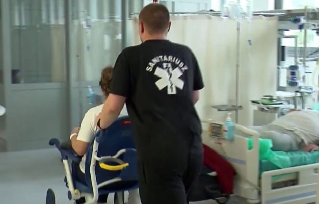 Mężczyzna pcha pacjenta na wózku na sali szpitalnej.