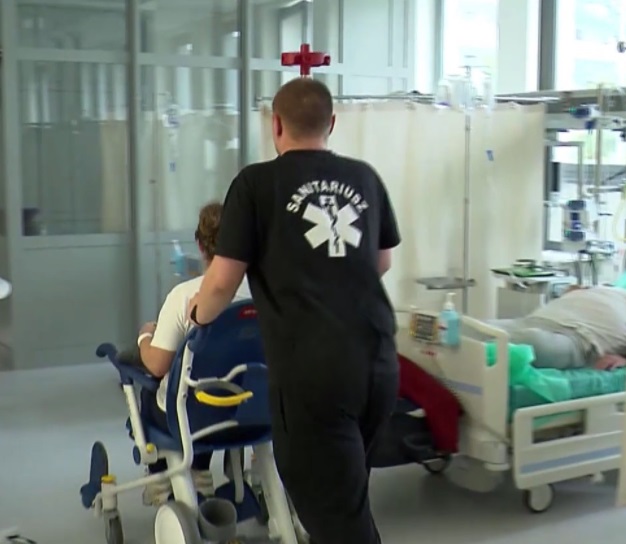 Mężczyzna pcha pacjenta na wózku na sali szpitalnej.