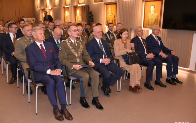 Relacja z Inauguracji Roku Akademickiego 2024/2025 w WIM-PIB. Dyrektor WIM na czele z innymi uczestnikami inauguracji siedzą i słuchają wykładu.