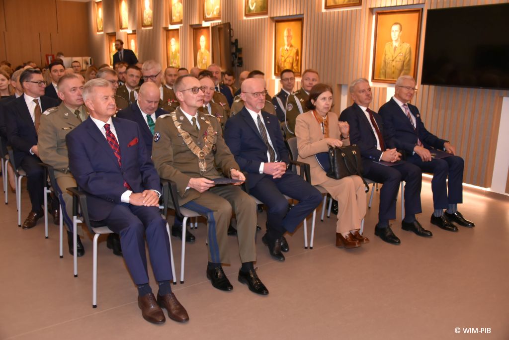 Relacja z Inauguracji Roku Akademickiego 2024/2025 w WIM-PIB. Dyrektor WIM na czele z innymi uczestnikami inauguracji siedzą i słuchają wykładu.