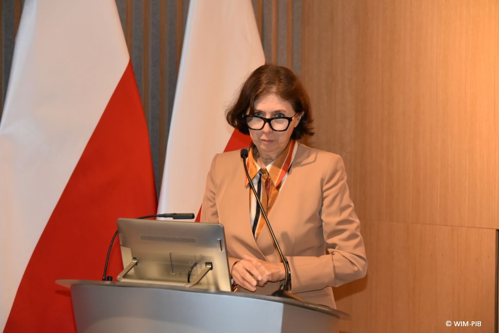 Relacja z Inauguracji Roku Akademickiego 2024/2025 w WIM-PIB. Prowadząca Inaugurację przy mównicy.