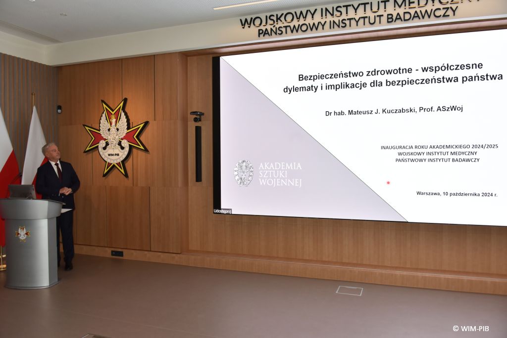 Relacja z Inauguracji Roku Akademickiego 2024/2025 w WIM-PIB. Prelegent prowadzi prezentację o bezpieczeństwie zdrowotnym.
