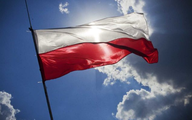 Flaga Polski na tle nieba, przez nią prześwituje słońce.
