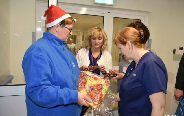 Zdjęcie kolorowe. Mikołajki w Wojskowym Instytucie Medycznym. Klinika Pediatryczna. Goście i pracownicy WIM z prezentami w rekach na korytarzu kliniki pediatrycznej.