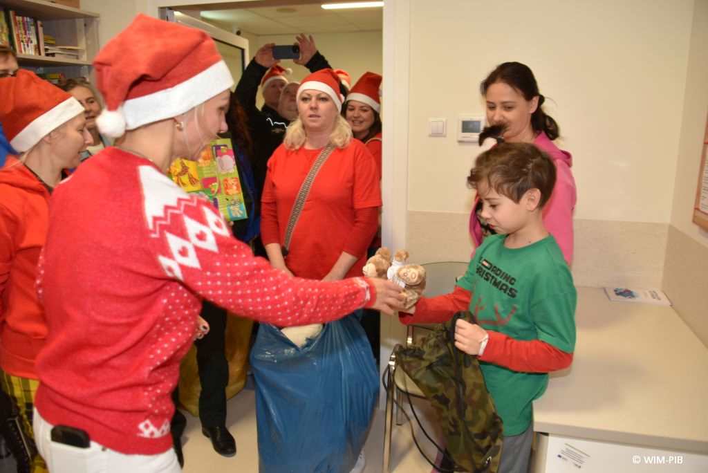 Zdjęcie kolorowe. Mikołajki w Wojskowym Instytucie Medycznym. Klinika Pediatryczna. Małgorzata Złotkowska wręcza dzieciom na sali szpitalnej prezenty.
