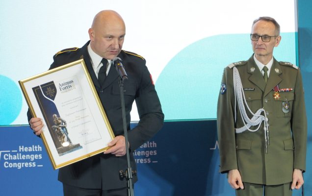 Paweł Marczak odbiera wyróżnienie Animus Fortis (Mężny Duch). W rękach trzyma wyróżnienie oprawione w złote ramy pochyla się nad mikrofonem aby wygłosić mowę