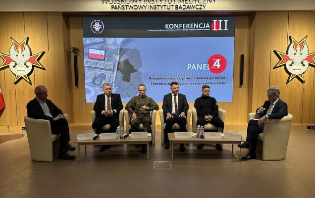 Paneliści siedzący w fotelach. Za nimi ogromny ekran z planszą konferencji.