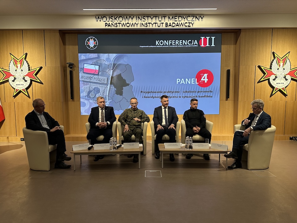 Paneliści siedzący w fotelach. Za nimi ogromny ekran z planszą konferencji.