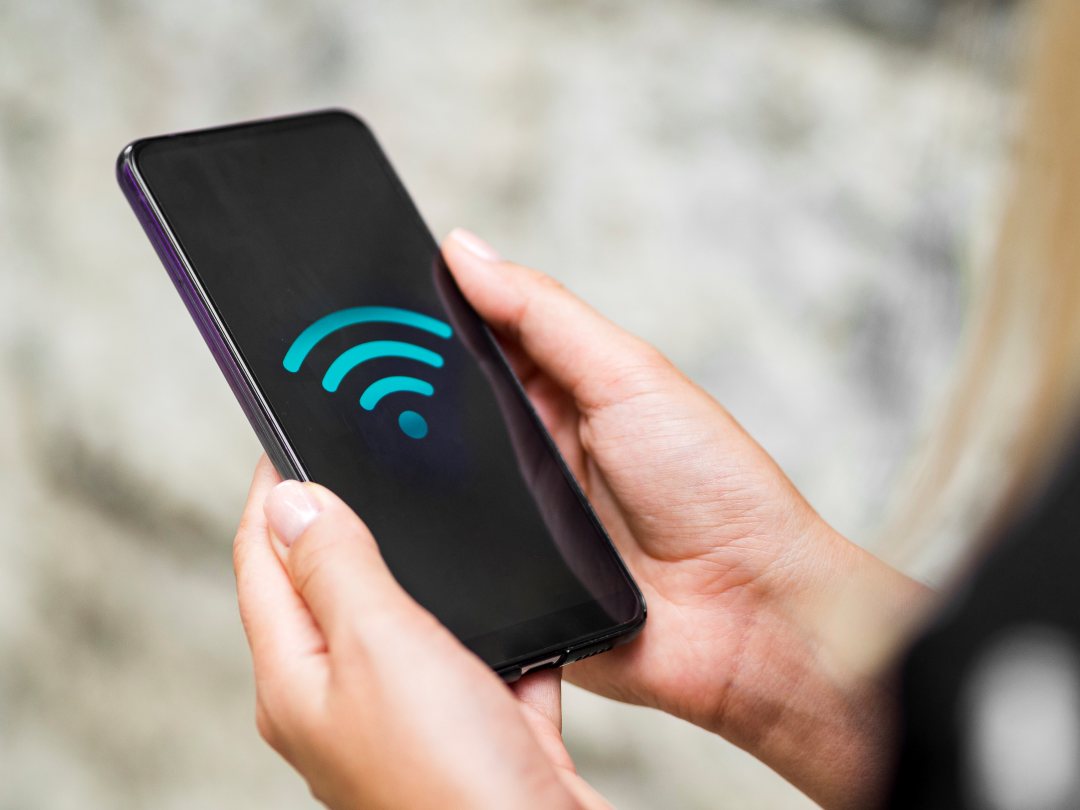 Telefon komórkowy w dłoniach z wyświetlonym na ekranie symbolem fi-fi.
