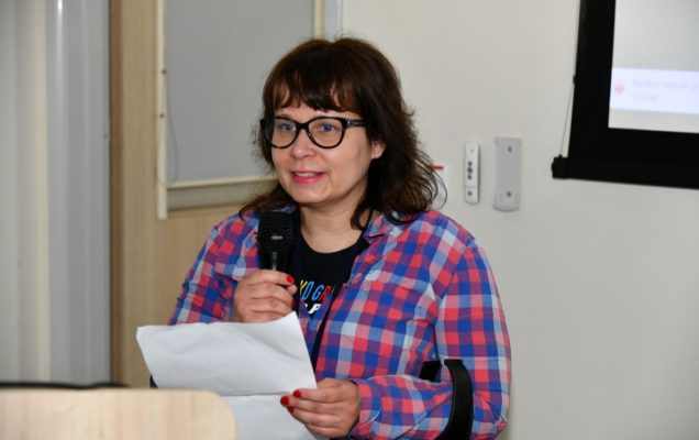dr Agata Kodroń przy mównicy z mikrofonem w ręku i notatkami podczas wykładu.