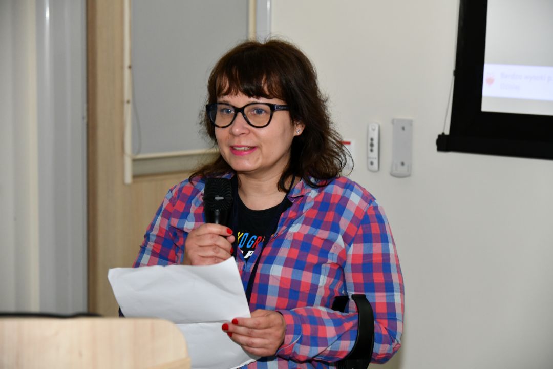 dr Agata Kodroń przy mównicy z mikrofonem w ręku i notatkami podczas wykładu.