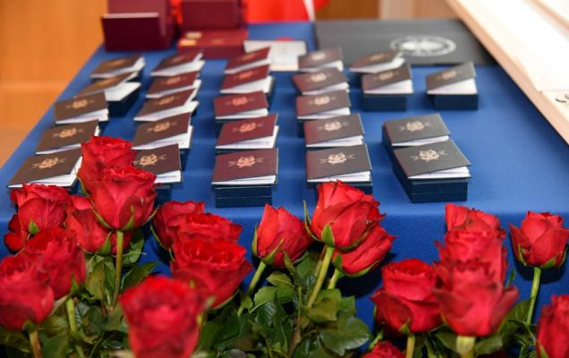 Pudełka z odznaczeniami na granatowym płótnie obok bukiet czerwonych róż.