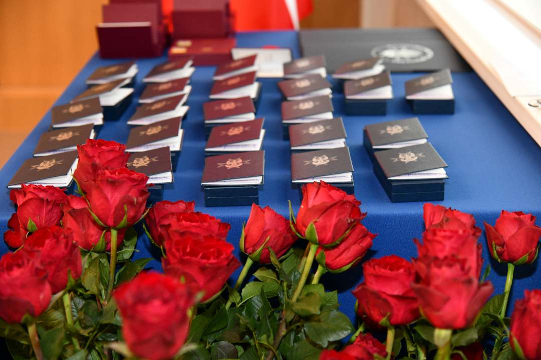 Pudełka z odznaczeniami na granatowym płótnie obok bukiet czerwonych róż.