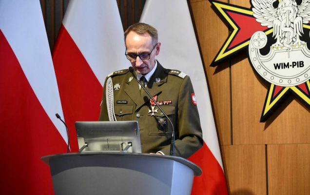 Dyrektor WIM przy mównicy, za nim trzy flagi polski i logo WIM.