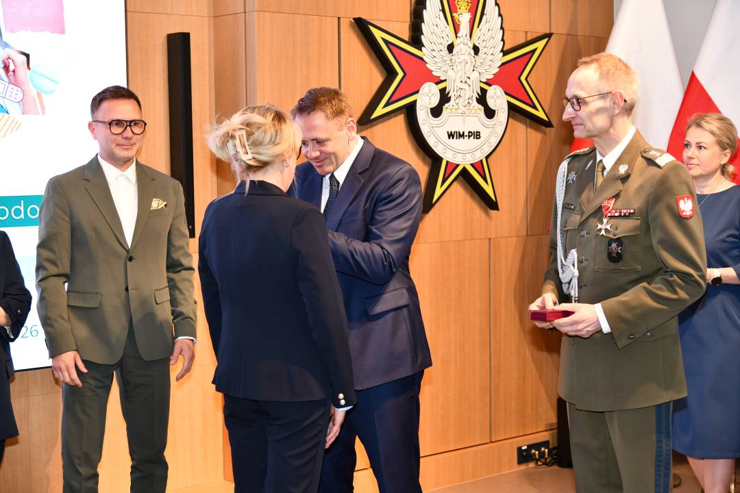 Mateusz Kotecki przypina kobiecie odznaczenie, obok stoi dyrektor WIM.