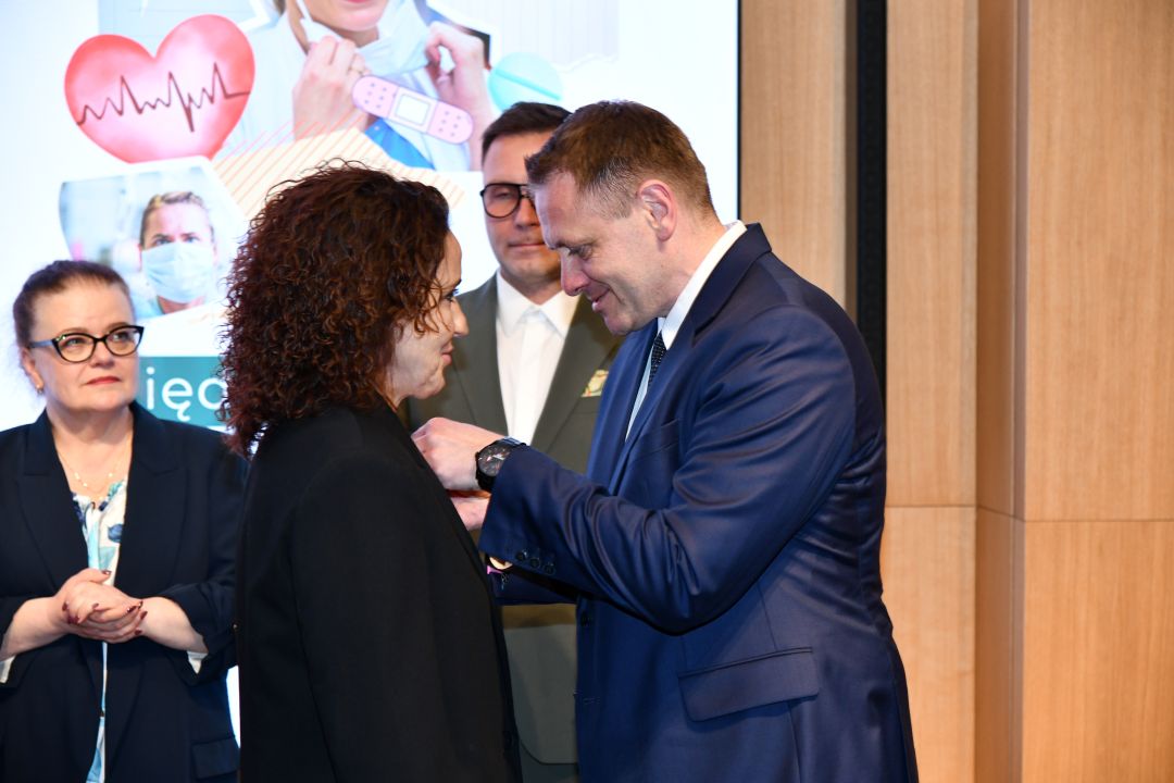 Mateusz Kotecki przypina kobiecie odznaczenie.