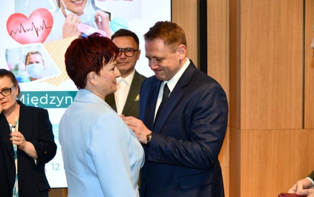 Mateusz Kotecki przypina kobiecie odznaczenie.