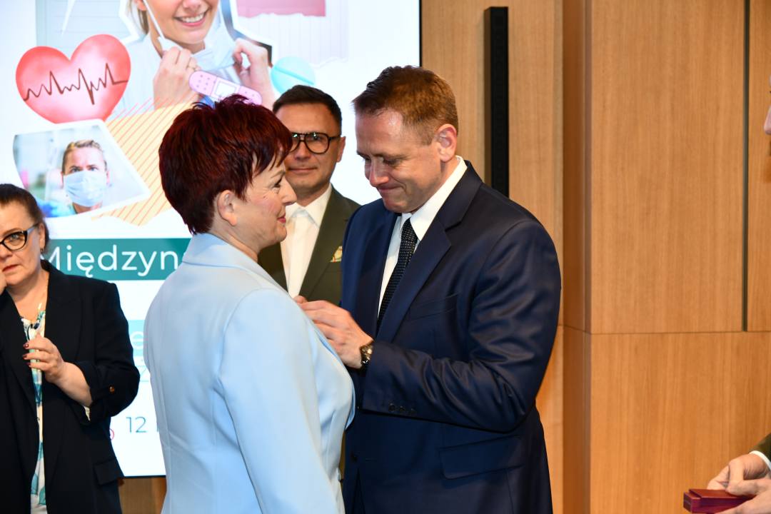 Mateusz Kotecki przypina kobiecie odznaczenie.