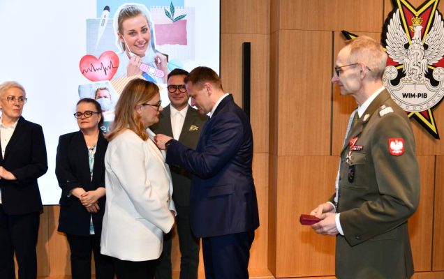 Mateusz Kotecki przypina kobiecie odznaczenie, obok stoi dyrektor WIM.