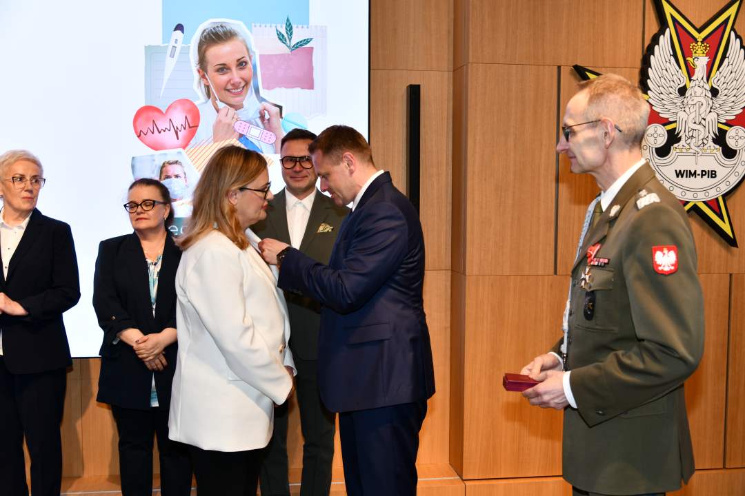 Mateusz Kotecki przypina kobiecie odznaczenie, obok stoi dyrektor WIM.