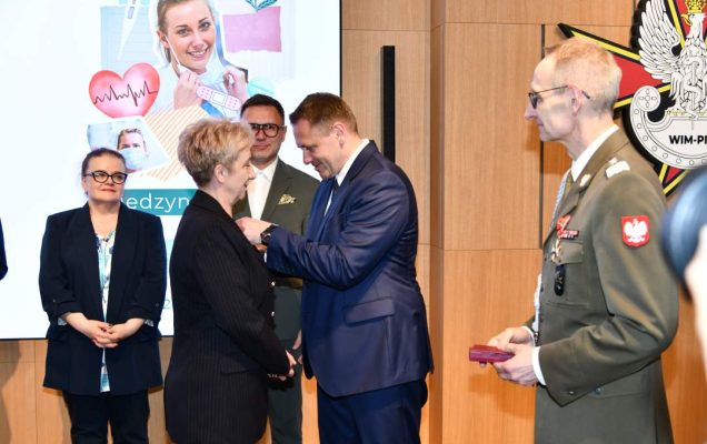 Mateusz Kotecki przypina kobiecie odznaczenie, obok stoi dyrektor WIM.