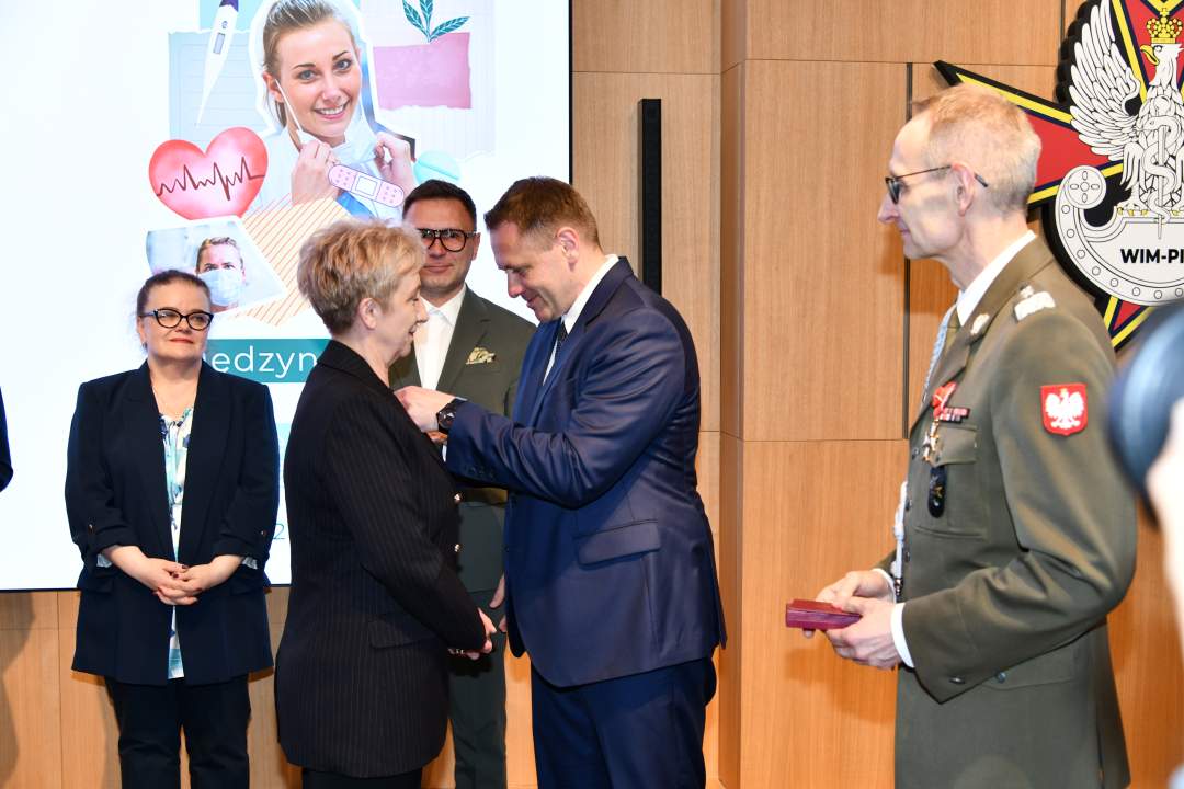 Mateusz Kotecki przypina kobiecie odznaczenie, obok stoi dyrektor WIM.