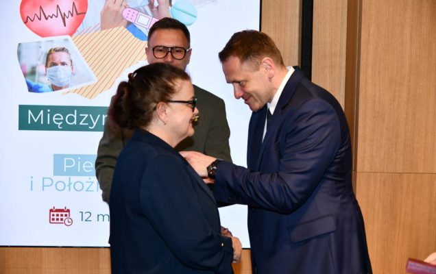 Mateusz Kotecki przypina kobiecie odznaczenie.