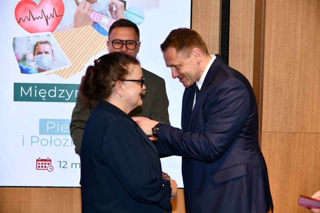 Mateusz Kotecki przypina kobiecie odznaczenie.