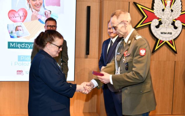 Dyrektor WIM wręcza pielęgniarce odznaczenie, obok stoi Mateusz Kotecki.