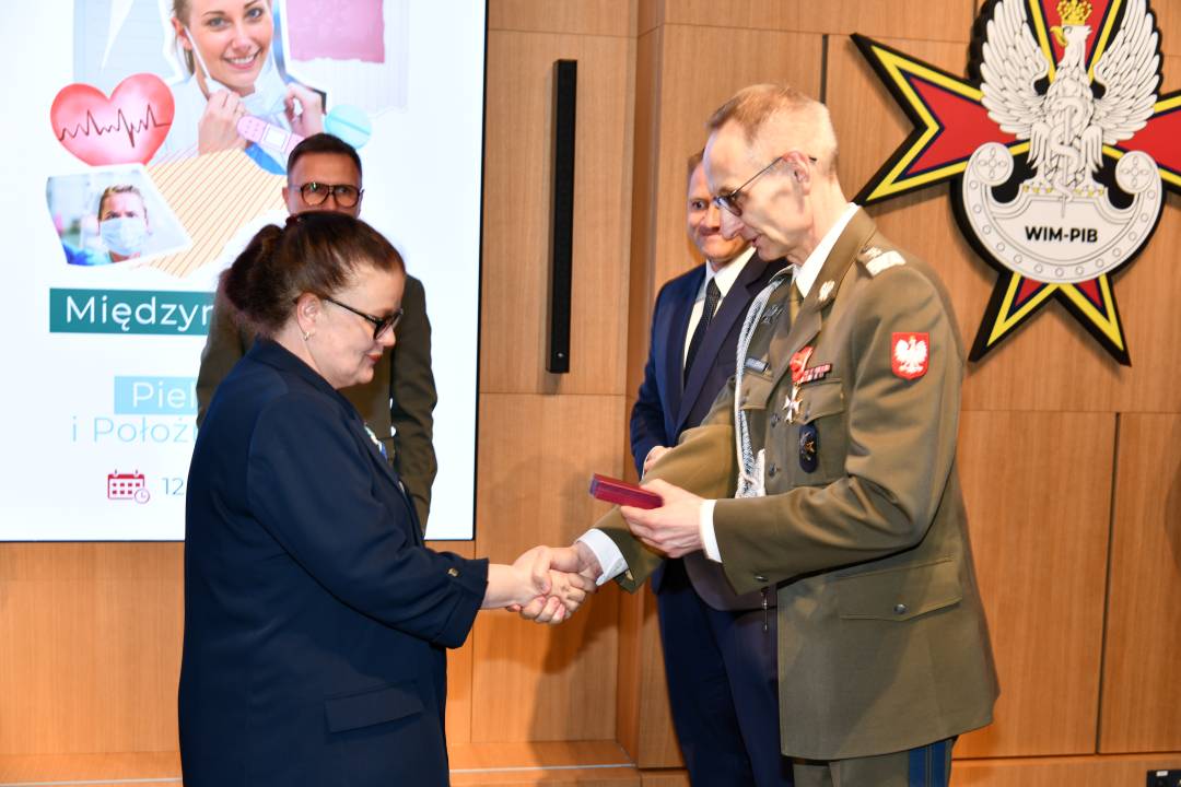 Dyrektor WIM wręcza pielęgniarce odznaczenie, obok stoi Mateusz Kotecki.