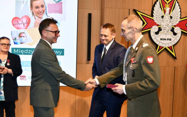 Dyrektor WIM wręcza mężczyźnie odznaczenie, obok stoi Mateusz Kotecki.