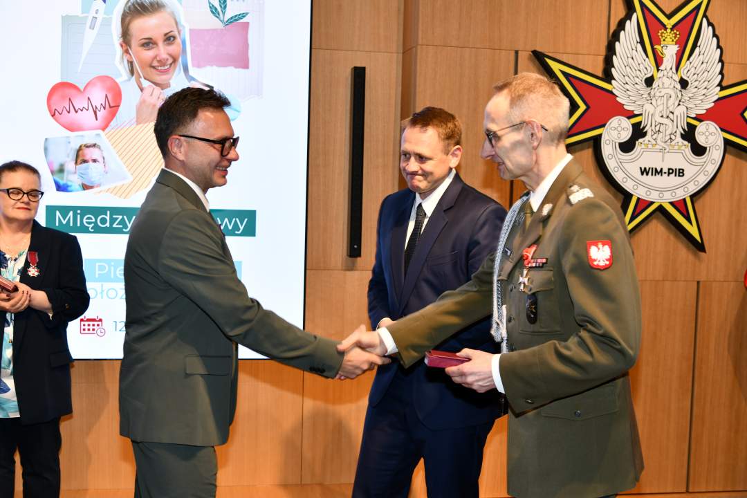 Dyrektor WIM wręcza mężczyźnie odznaczenie, obok stoi Mateusz Kotecki.