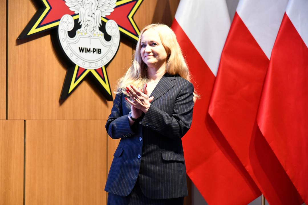 Ministra Zdrowia bije brawo na tle flagi Polski.