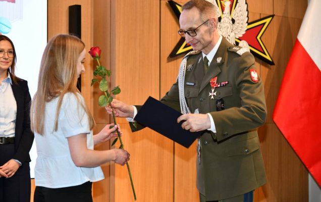 Dyrektor WIM wręcza pielęgniarce czerwoną różę i odznaczenie.