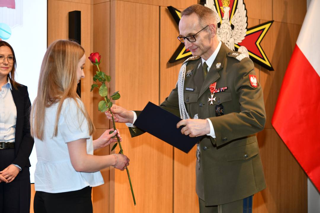 Dyrektor WIM wręcza pielęgniarce czerwoną różę i odznaczenie.