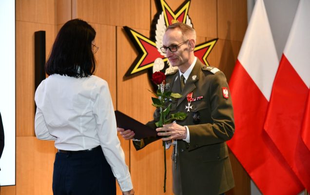 Dyrektor WIM wręcza pielęgniarce czerwoną różę i odznaczenie.