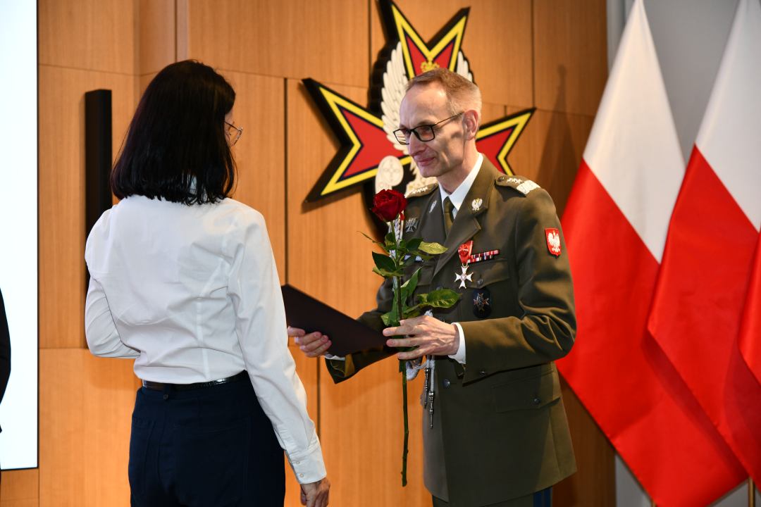 Dyrektor WIM wręcza pielęgniarce czerwoną różę i odznaczenie.