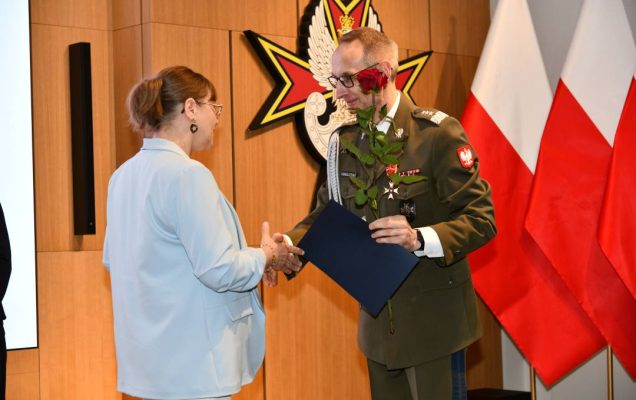Dyrektor WIM wręcza pielęgniarce czerwoną różę i odznaczenie.