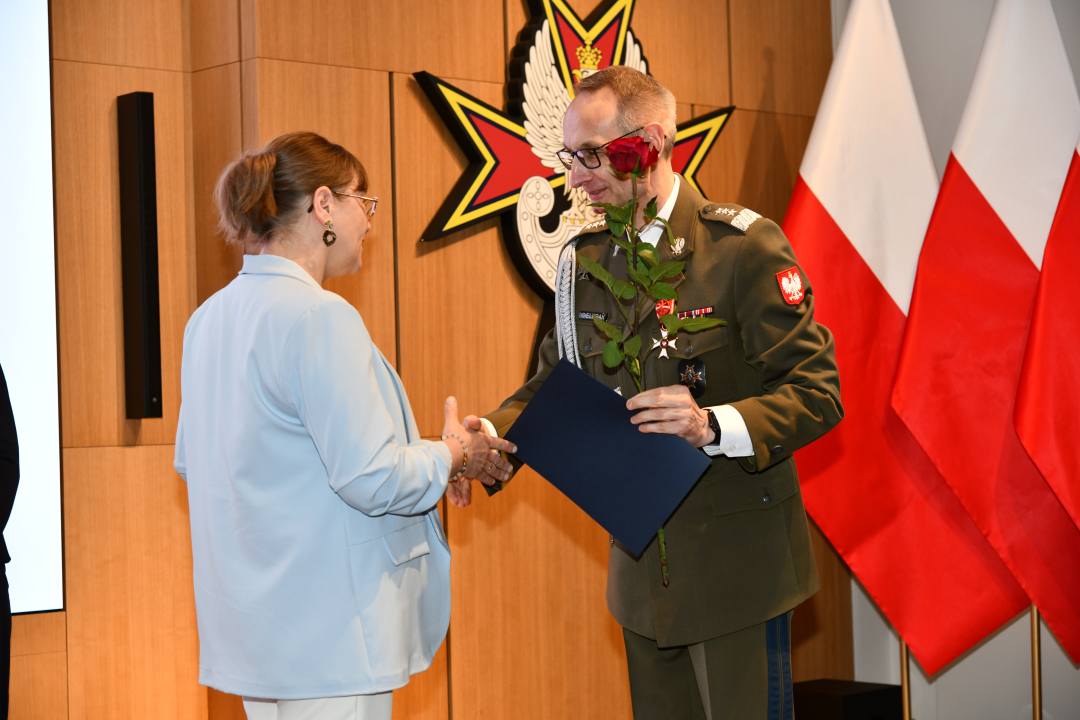 Dyrektor WIM wręcza pielęgniarce czerwoną różę i odznaczenie.