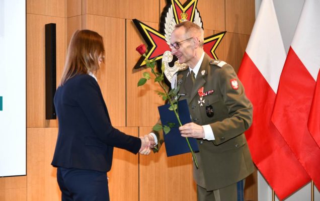 Dyrektor WIM wręcza pielęgniarce czerwoną różę i odznaczenie.