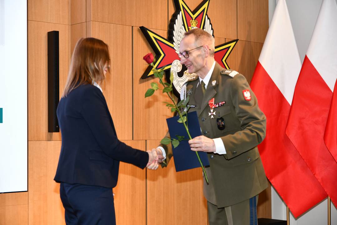 Dyrektor WIM wręcza pielęgniarce czerwoną różę i odznaczenie.