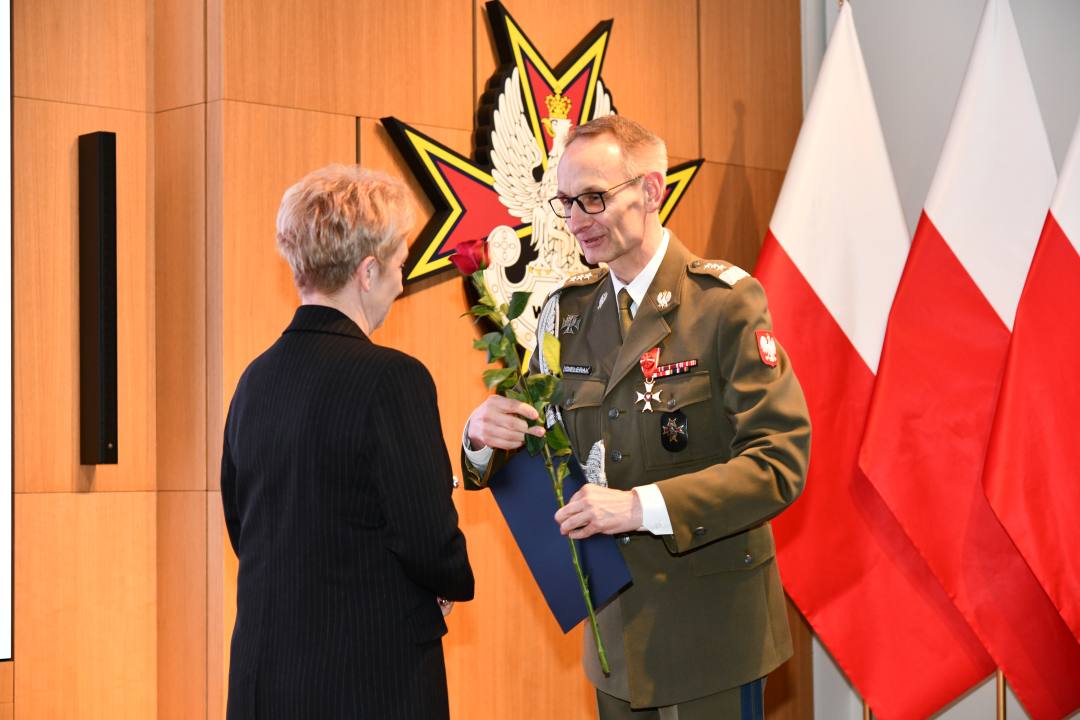 Dyrektor WIM wręcza pielęgniarce czerwoną różę i odznaczenie.